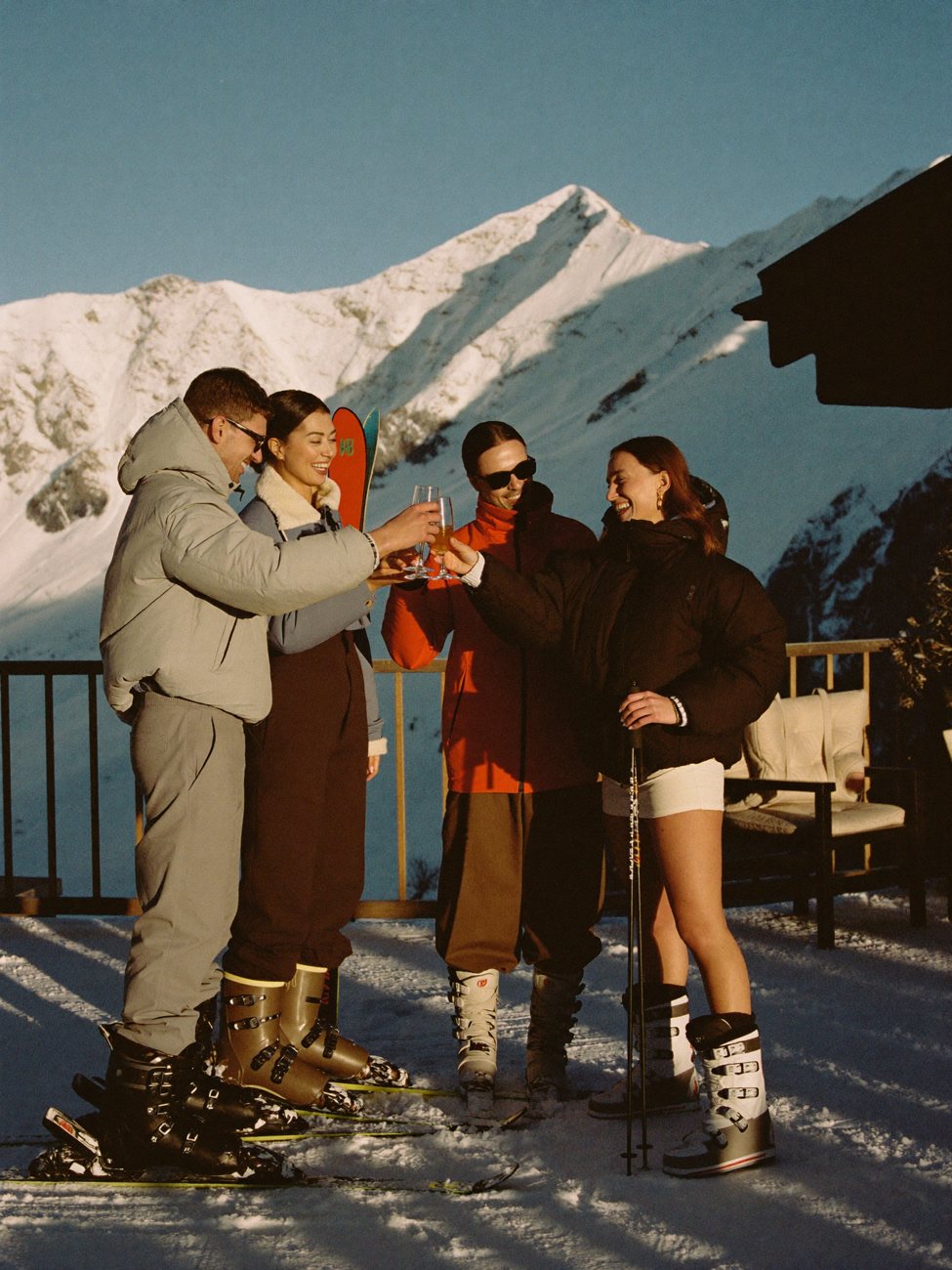 Friends toasting drinks on a snowy chalet terrace at golden hour